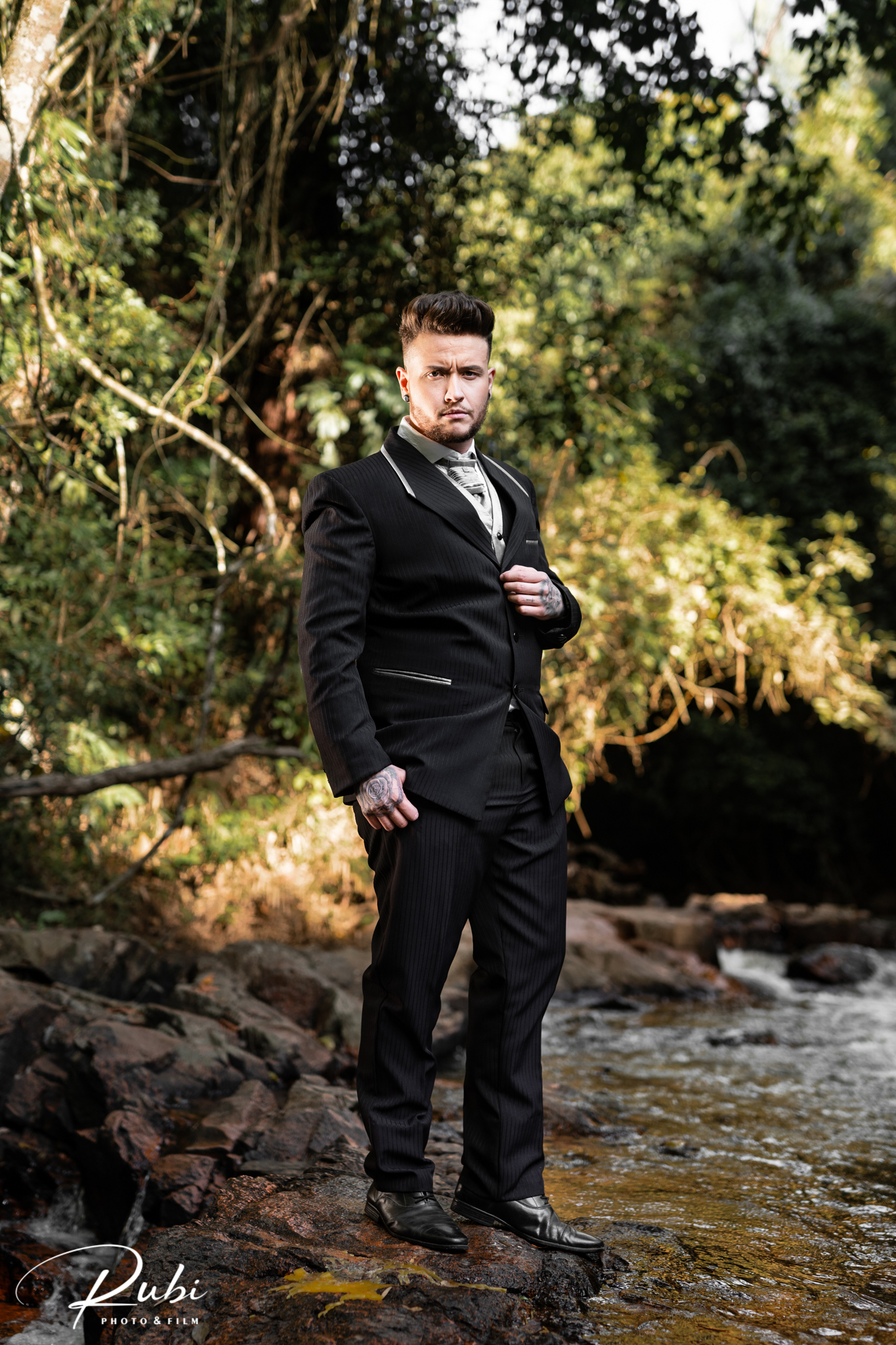 Noivo de corpo inteiro usando terno preto em cenário natural